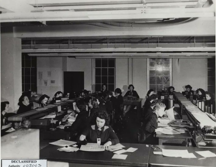 Women serving as wartime human computers work through calculations by hand and with desk machines.